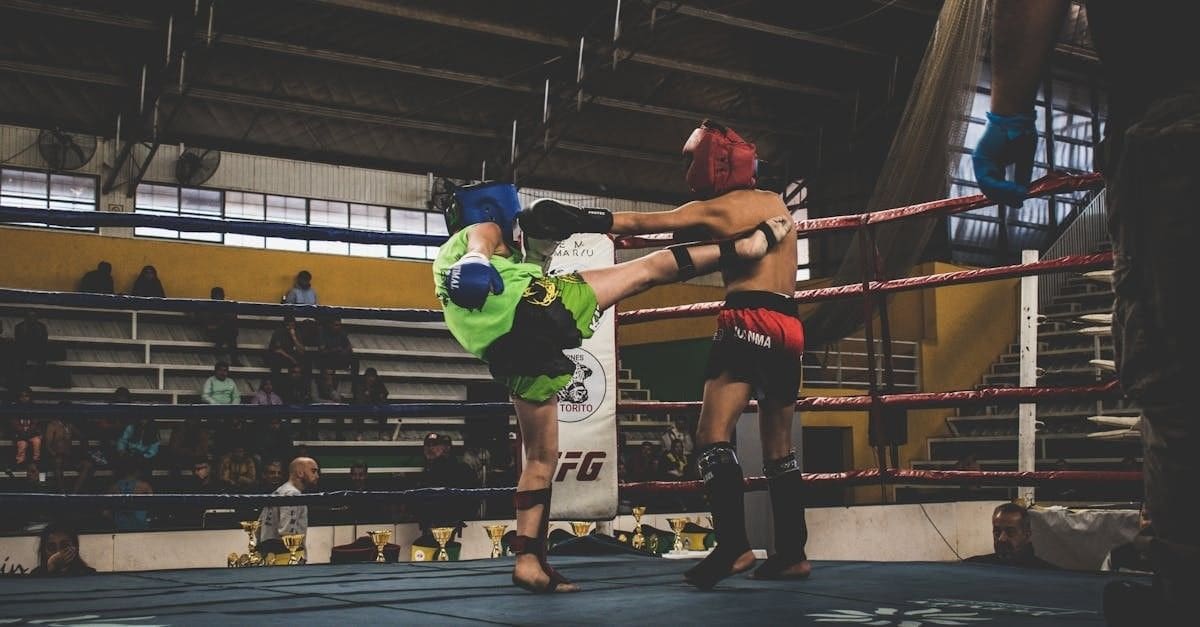 A competitive muay thai match where a fighter in green lands a high kick on an opponent in red.