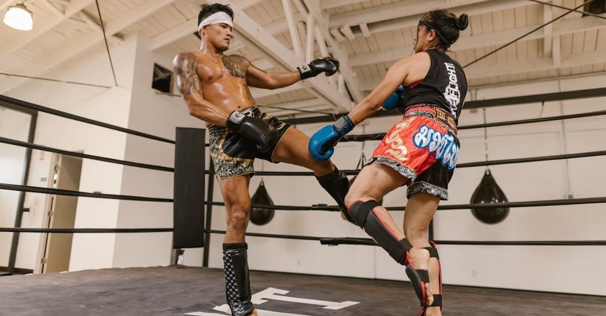 A male muay thai fighter executing a right roundhouse kick against a female opponent blocking the strike.